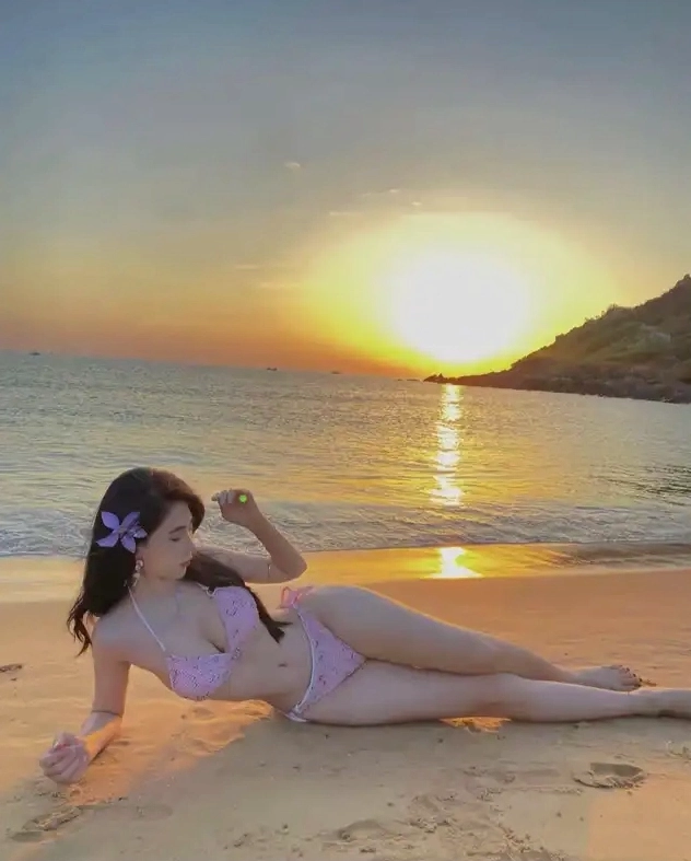Cô gái với đường cong hút mắt nằm nghiêng trên bãi cát mặc bikini hồng thư thái ngắm mặt trời lặn